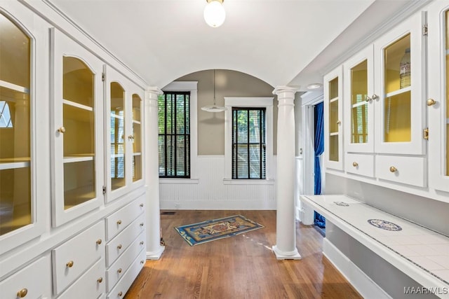 interior space featuring vaulted ceiling, a wainscoted wall, decorative columns, and wood finished floors