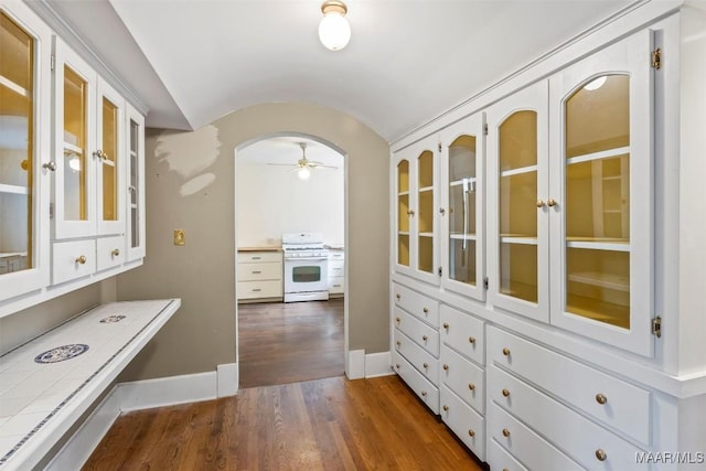 kitchen featuring tile counters, white gas stove, dark wood finished floors, vaulted ceiling, and arched walkways