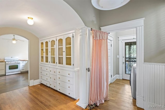 corridor with arched walkways, light wood-style floors, and decorative columns