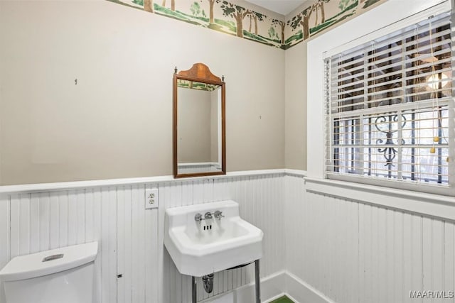 half bathroom with a sink, toilet, and wainscoting