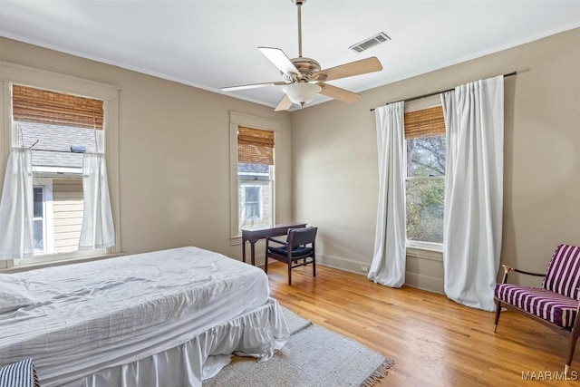 bedroom with baseboards, visible vents, light wood-style flooring, ceiling fan, and crown molding