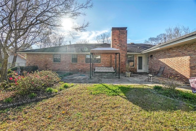 rear view of property featuring brick siding, a lawn, and a patio