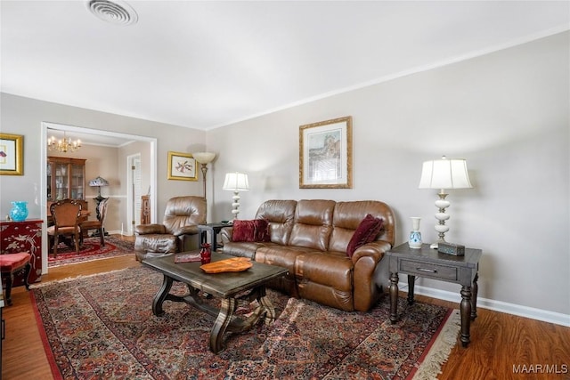 living room featuring wood finished floors, baseboards, visible vents, ornamental molding, and a chandelier