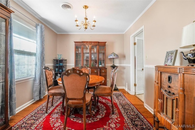 dining space featuring wood finished floors, visible vents, baseboards, ornamental molding, and a chandelier