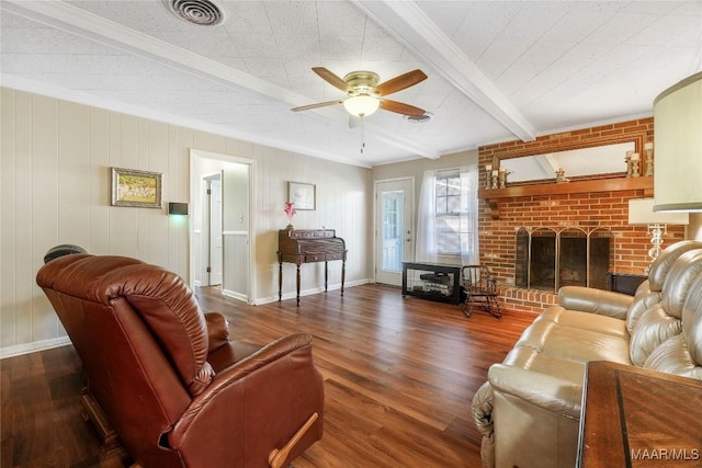 living area featuring visible vents, beam ceiling, a ceiling fan, wood finished floors, and a brick fireplace