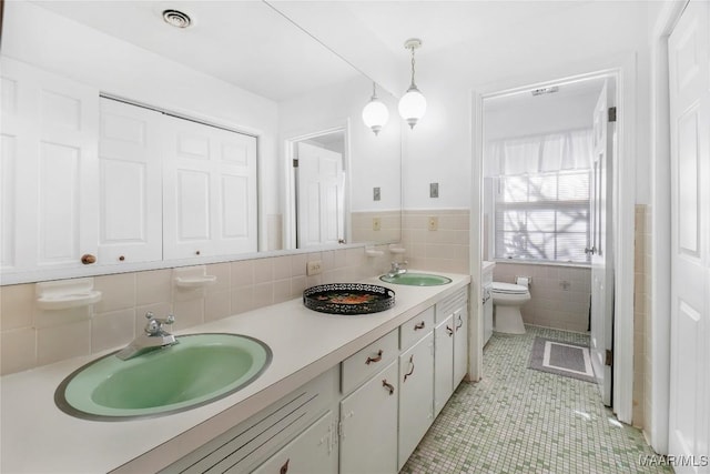 full bathroom with visible vents, toilet, tile walls, and a sink