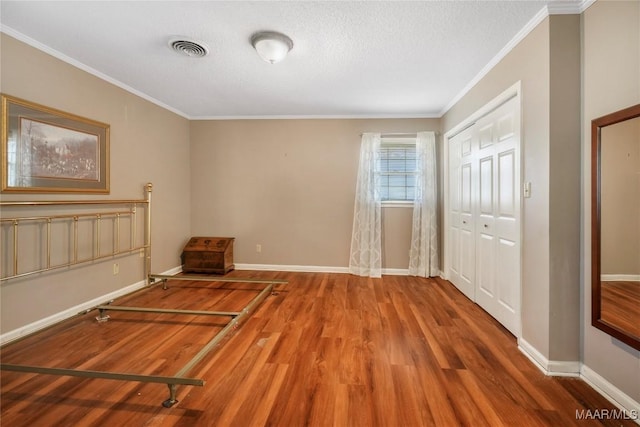 interior space featuring visible vents, wood finished floors, a closet, crown molding, and baseboards