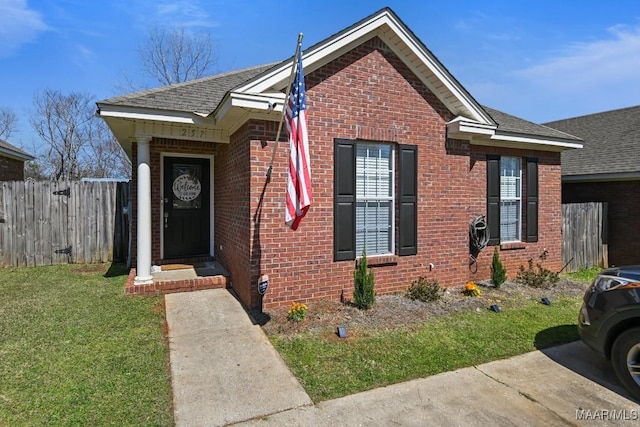 bungalow-style home featuring a front lawn, fence, brick siding, and a shingled roof