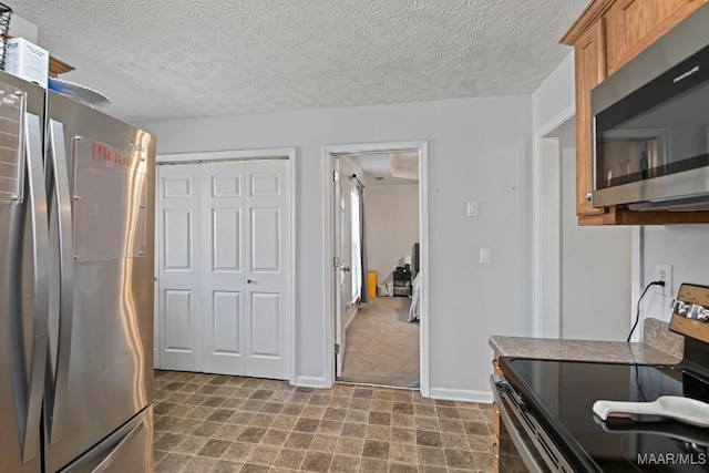 kitchen featuring a textured ceiling, stainless steel appliances, dark floors, brown cabinetry, and baseboards