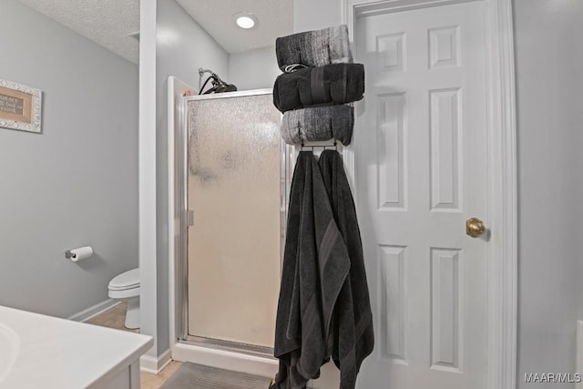 bathroom featuring toilet, a textured ceiling, a shower stall, baseboards, and vanity