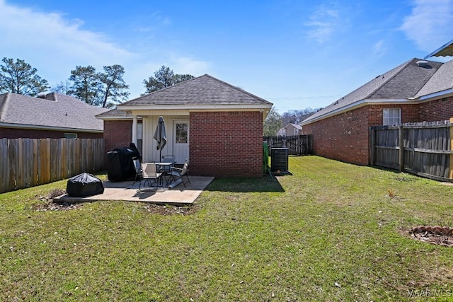 rear view of house with brick siding, roof with shingles, a lawn, a fenced backyard, and a patio area