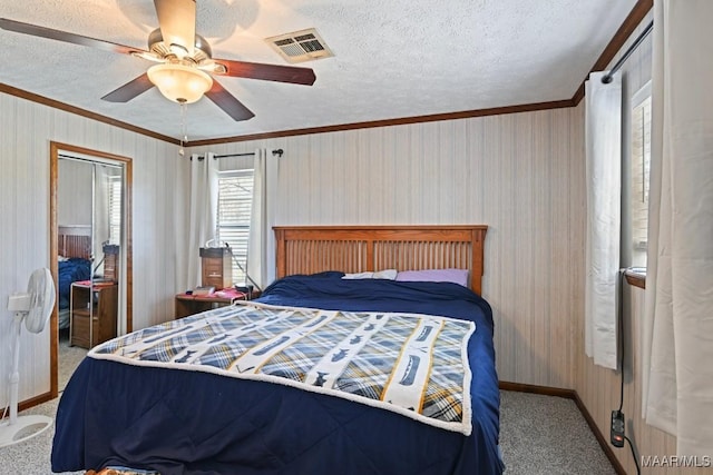 carpeted bedroom with visible vents, crown molding, baseboards, ceiling fan, and a textured ceiling