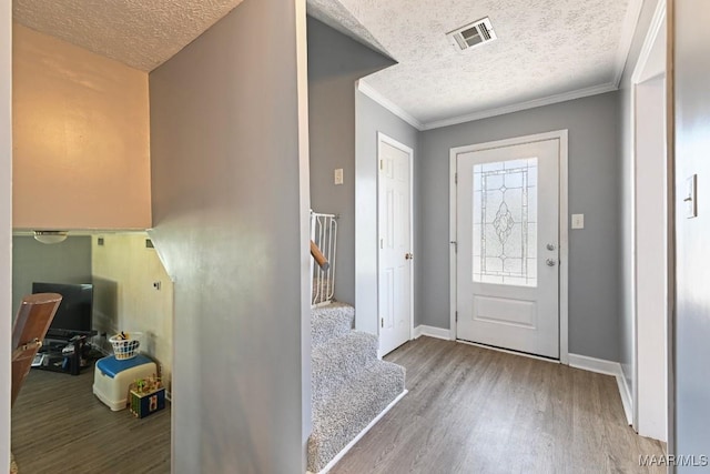 foyer entrance with ornamental molding, wood finished floors, visible vents, and a textured ceiling