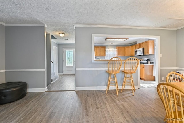 kitchen featuring light wood-type flooring, stainless steel appliances, a kitchen breakfast bar, and ornamental molding