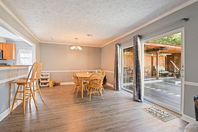 dining space with a notable chandelier, a textured ceiling, wood finished floors, crown molding, and baseboards