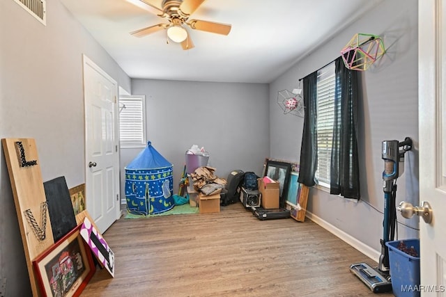 rec room with a ceiling fan, wood finished floors, visible vents, and baseboards