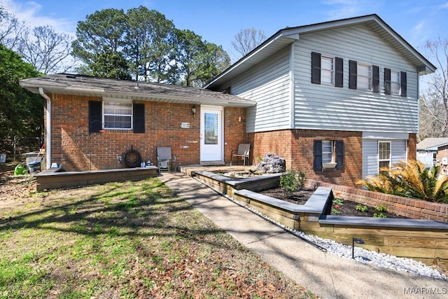 tri-level home featuring a garden, brick siding, and a front yard