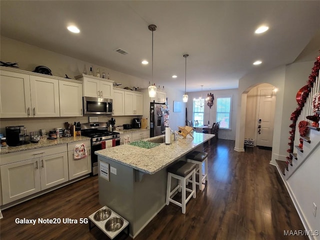 kitchen featuring visible vents, an island with sink, white cabinetry, stainless steel appliances, and arched walkways