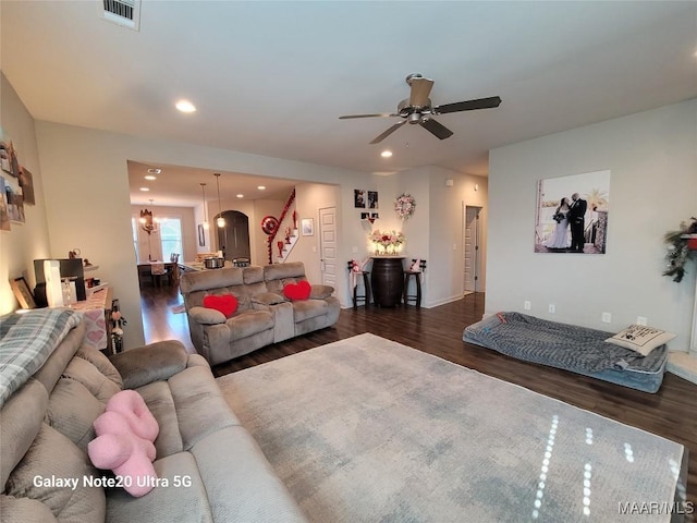 living area with visible vents, dark wood-type flooring, ceiling fan with notable chandelier, recessed lighting, and stairs