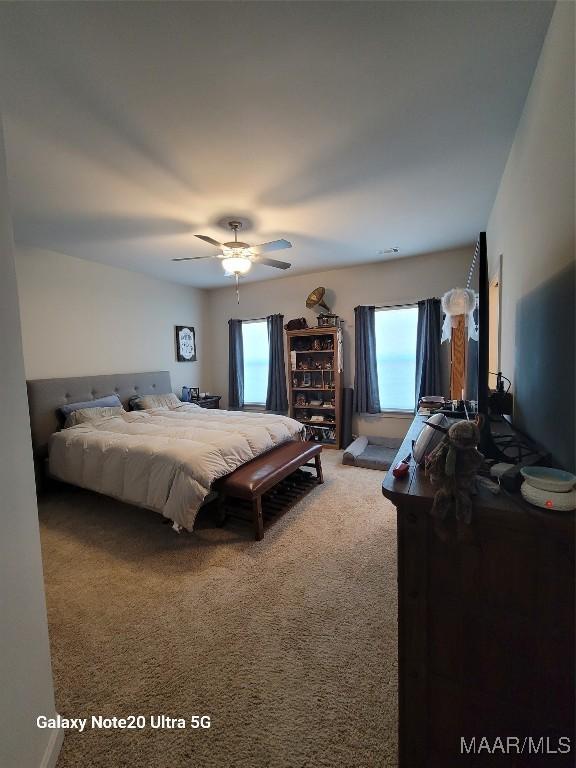 carpeted bedroom featuring visible vents, multiple windows, and ceiling fan