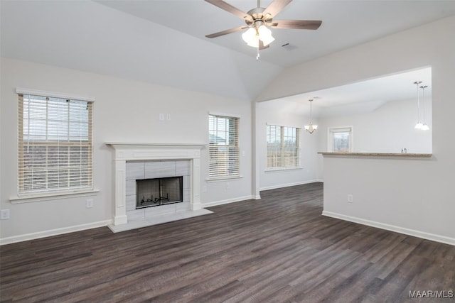 unfurnished living room with baseboards, a tiled fireplace, vaulted ceiling, ceiling fan with notable chandelier, and wood finished floors