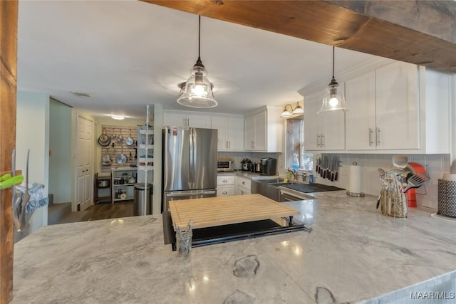 kitchen with backsplash, light stone countertops, freestanding refrigerator, hanging light fixtures, and white cabinets