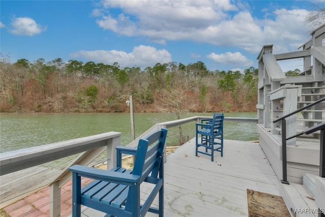 dock area featuring stairway, a deck with water view, and a wooded view