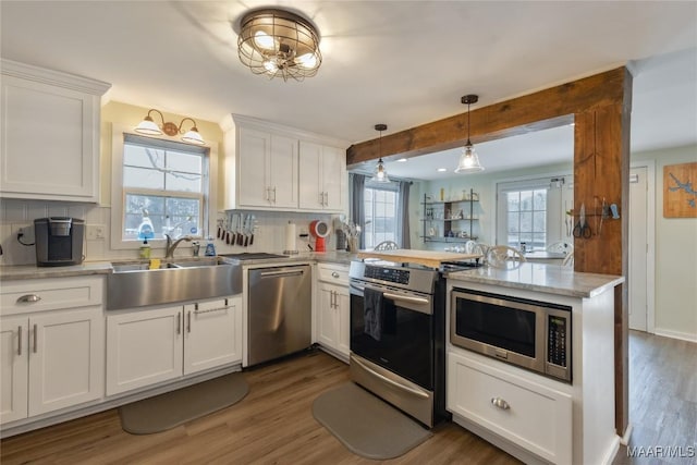 kitchen featuring a sink, wood finished floors, white cabinetry, appliances with stainless steel finishes, and a peninsula