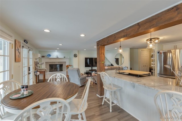 dining room with recessed lighting, beamed ceiling, wood finished floors, and a glass covered fireplace