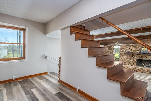 staircase featuring a stone fireplace, baseboards, and wood finished floors