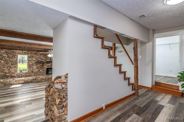 stairway with visible vents, a textured ceiling, wood finished floors, a fireplace, and baseboards