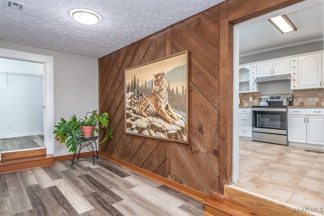 interior space with light wood-style flooring, visible vents, wood walls, and a textured ceiling