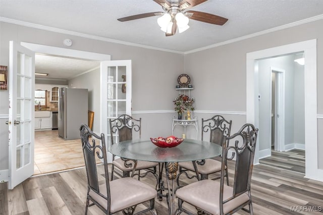 dining area featuring a ceiling fan, a textured ceiling, french doors, light wood-style floors, and crown molding