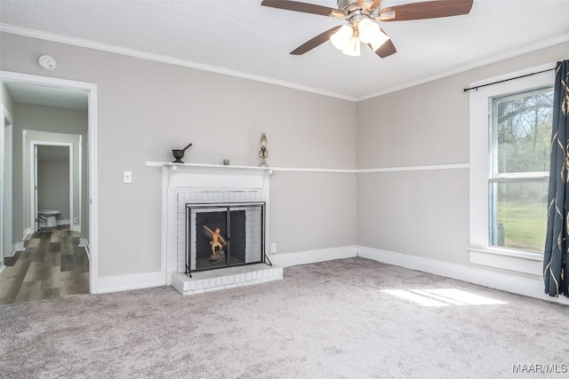 unfurnished living room with a brick fireplace, crown molding, baseboards, carpet flooring, and a ceiling fan