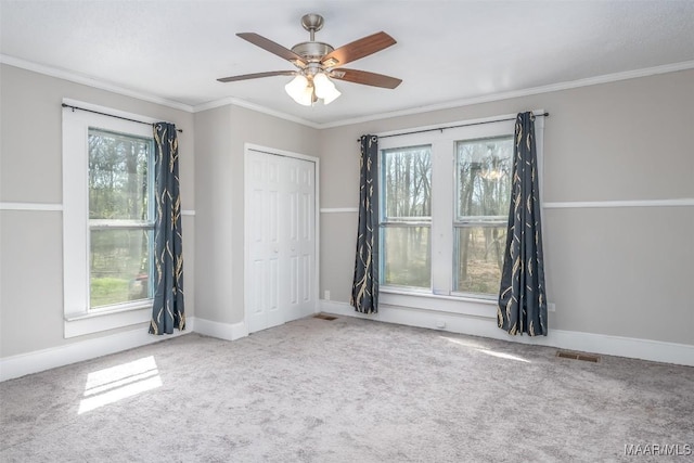 carpeted empty room with a wealth of natural light, visible vents, and ornamental molding