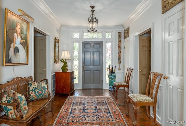 entrance foyer with dark wood finished floors, a decorative wall, a chandelier, and ornamental molding