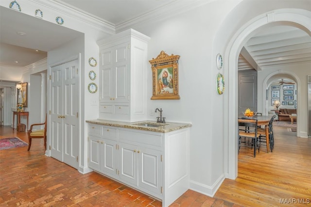 bar featuring ornamental molding, baseboards, arched walkways, and a sink