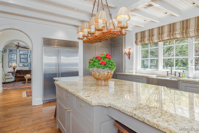 kitchen with beamed ceiling, stainless steel built in fridge, light wood-style flooring, ceiling fan with notable chandelier, and arched walkways