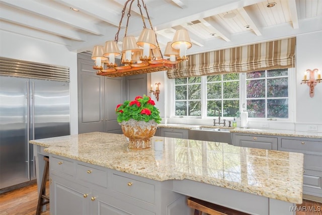 kitchen featuring light stone counters, light wood-style flooring, gray cabinetry, built in fridge, and beamed ceiling