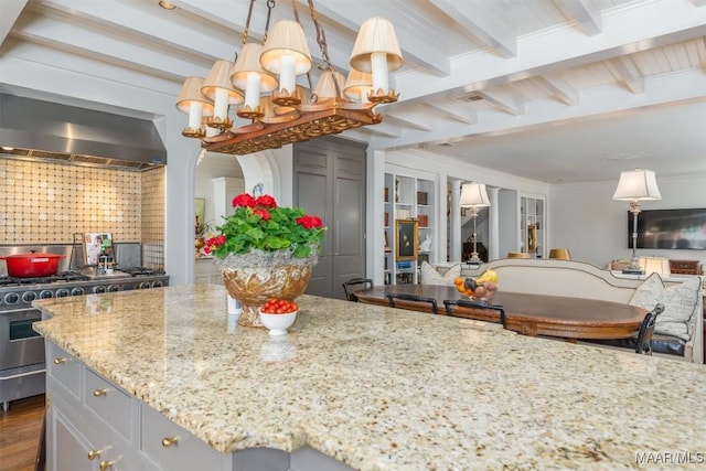 kitchen featuring beam ceiling, stainless steel gas range, light stone counters, and ornamental molding