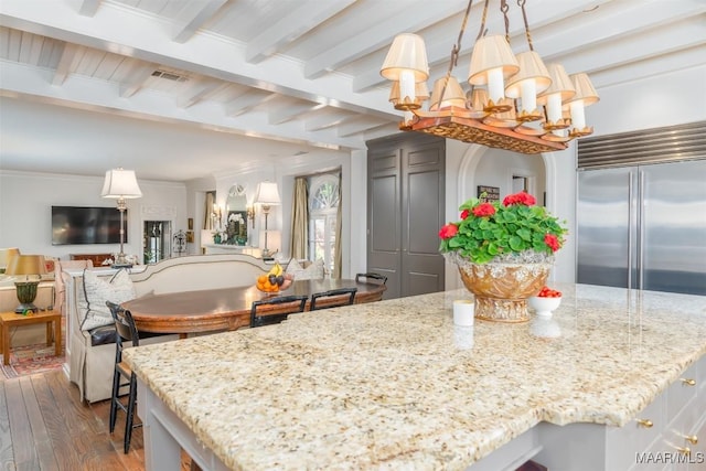 kitchen featuring beam ceiling, hardwood / wood-style flooring, light stone counters, and a kitchen island