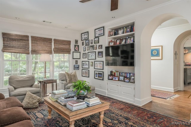 living room featuring arched walkways, visible vents, crown molding, and wood finished floors