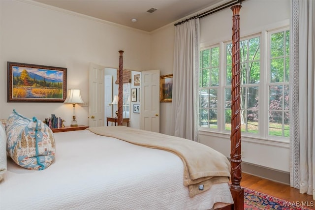 bedroom featuring multiple windows, wood finished floors, visible vents, and ornamental molding