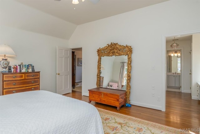 bedroom featuring lofted ceiling, wood finished floors, baseboards, and a sink