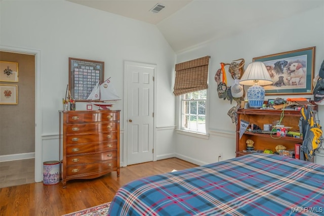 bedroom featuring visible vents, baseboards, lofted ceiling, and wood finished floors