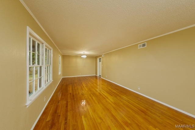 empty room featuring an inviting chandelier, wood finished floors, visible vents, and a textured ceiling