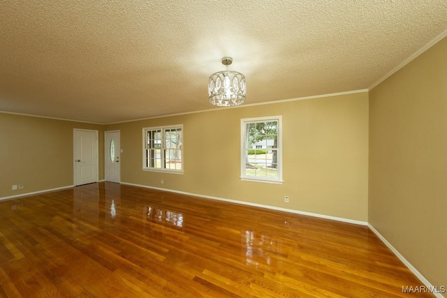 spare room featuring baseboards, a notable chandelier, wood finished floors, and ornamental molding