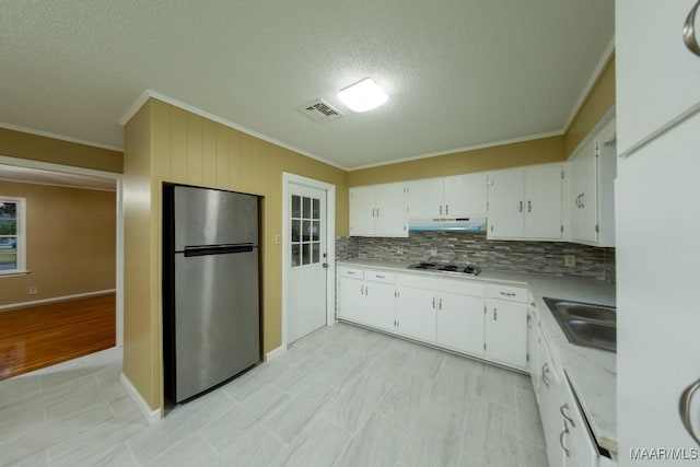 kitchen with freestanding refrigerator, a sink, cooktop, light countertops, and under cabinet range hood