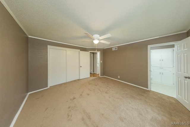 unfurnished bedroom featuring a closet, a textured ceiling, light carpet, and ornamental molding