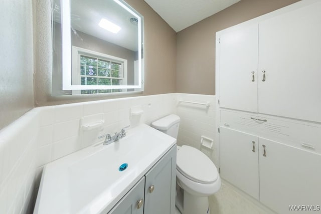 half bath with tile walls, a wainscoted wall, toilet, and vanity